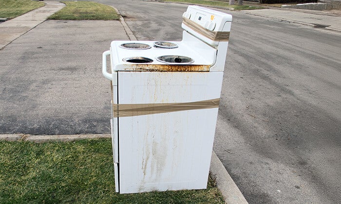 1-800-GOT-JUNK? hauls away an old stove with an appliance dolly.
