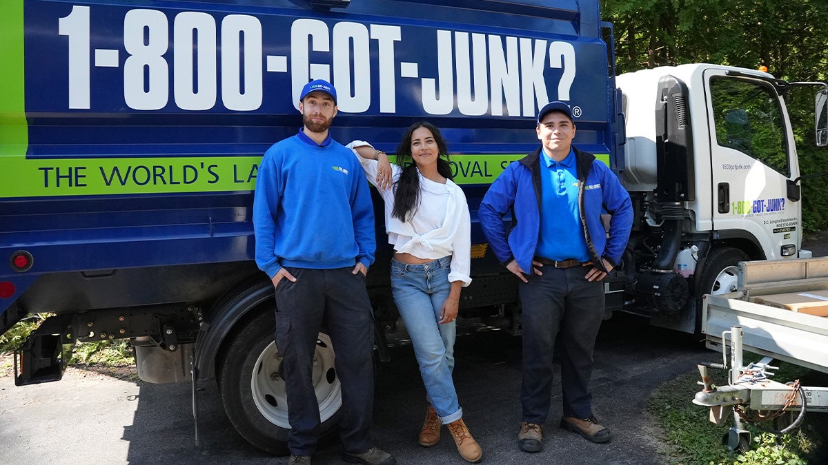 A woman and two 1-800-GOT-JUNK Truck Team Members smiling in front of the truck.